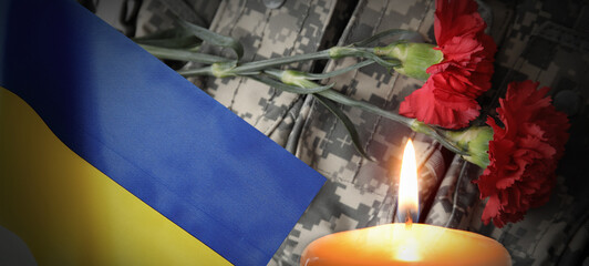 Burning candle and flag of Ukraine against flowers on military uniform. Honoring of fallen Ukrainian soldiers