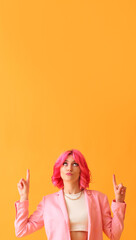 Stylish woman with bright pink hair pointing at something on yellow background