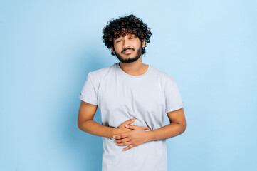 Problems with the esophagus, stomach ache. Indian guy in casual wear hunching and holding his...