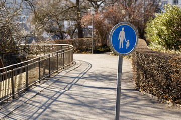 blue footpath sign, traffic sign, white painted man with child on blue background: pedestrians and users of vehicle-like devices must use the path. concrete path with railing in the background
