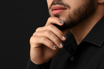 Fototapeta na wymiar Man with stylish manicure touching his face on black background, closeup