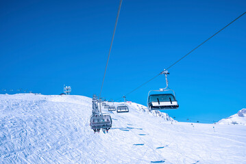 Ski lift moving over snow covered landscape against clear blue sky