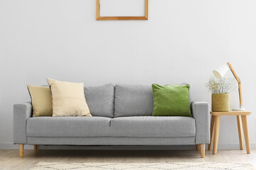 Grey sofa, table with gypsophila flowers in basket and lamp near light wall