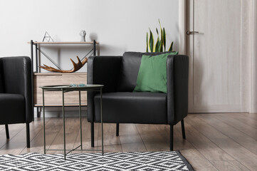 Black armchair with green pillow and table in interior of modern living room
