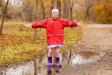 Happy little girl with rubber boots jumping in puddle outdoors