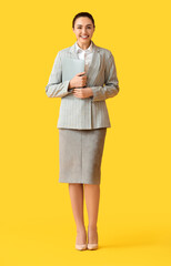 Pretty young businesswoman with folder on yellow background