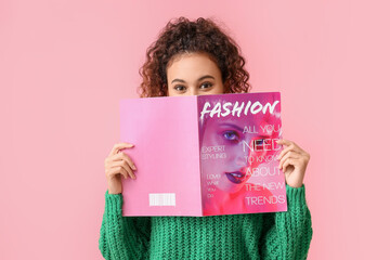 Young African-American woman in green sweater reading magazine on pink background - obrazy, fototapety, plakaty