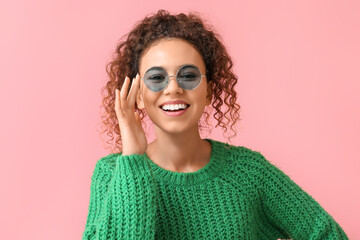 Young African-American woman in stylish sunglasses on pink background