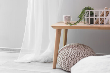 Basket with books, houseplant and cup on wooden table near light wall