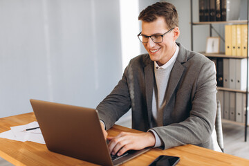 Modern smiling man, office worker working on laptop