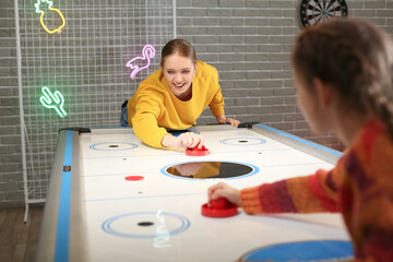 Woman and her little daughter playing air hockey indoors