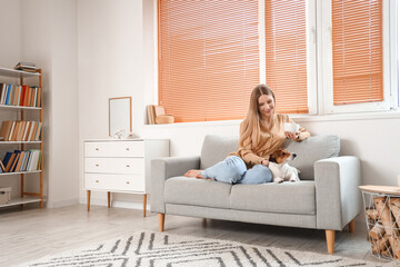 Young woman with cup of tea and Jack Russel terrier sitting on grey sofa at home