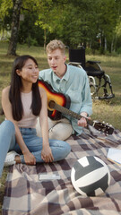 A disabled young guy in a blue shirt is playing guitar and singing songs for his girlfriend in tha...