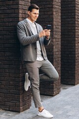 Fototapeta na wymiar Modern handsome smiling man standing by the wall on the street holding a phone
