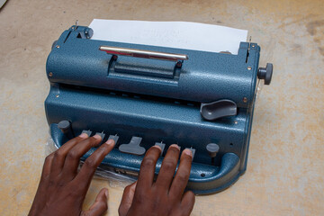 Close-up of a black blind person typing on a braille printer