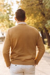 Modern handsome man in yellow and white clothes posing in the park at sunset