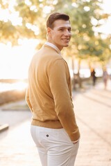 Modern handsome smiling man in yellow and white clothes posing in the park at sunset