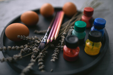 Multicolour paints and brushes on the plate with eggs. Colouring eggs for easter holiday concept.
