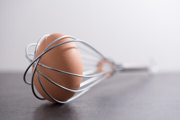 Fototapeta na wymiar A brown chicken egg trapped in a wire whisk kitchen utensil
