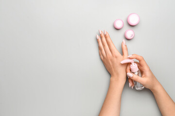 Woman with beautiful manicure applying sanitizer on grey background