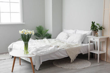 Interior of light bedroom with daffodils in vase and houseplants