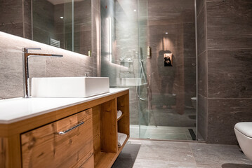 White sink on wooden cabinet. Shower cabin with glass doors. Interior of modern bathroom in hotel