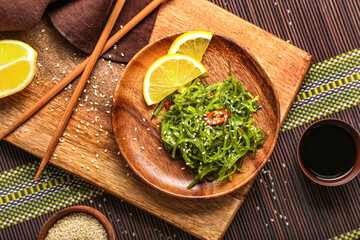 Plate with healthy seaweed salad, lemon and sauce on green background