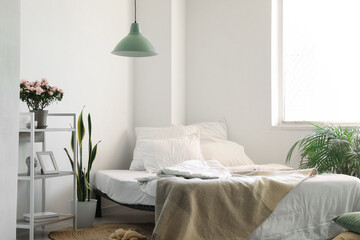 Comfortable bed, shelf unit and houseplants near light wall in room interior