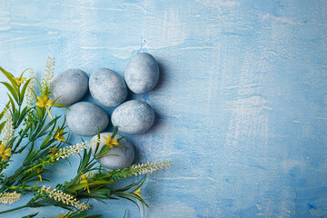 Painted Easter eggs on blue background with yellow flowers. Spring holiday, symbolic food. Top view, copy space.