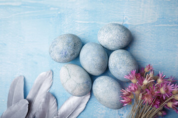Painted Easter eggs on blue background with purple flowers and feathers. Spring holiday symbol. Copy space, top view