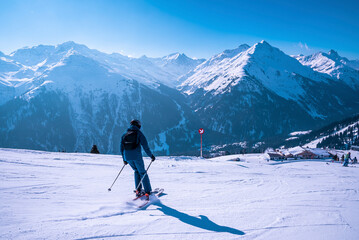 Skier skiing on snow covered landscape. Scenic mountain range against blue sky. Tourist enjoying adventure sport. - obrazy, fototapety, plakaty
