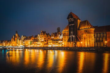 Obraz premium Beautiful architecture of the old town in Gdansk by the Motlawa river with a historic port crane at night. Poland, November 2021