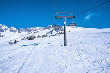 Fototapeta na wymiar Chairlift moving over snow covered mountain. Ski lift reaching towards range against blue sky. Scenic view of alps.