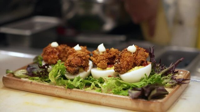 Chef dollops aioli on fried oyster topped deviled eggs, places bottle in background, close up slow motion slider 4K