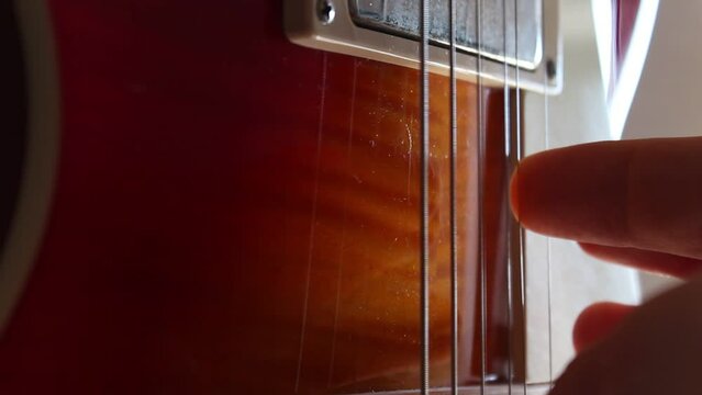 Fingers picking the strings of a Les Paul electric guitar in cherry sunburst. Static close up shot