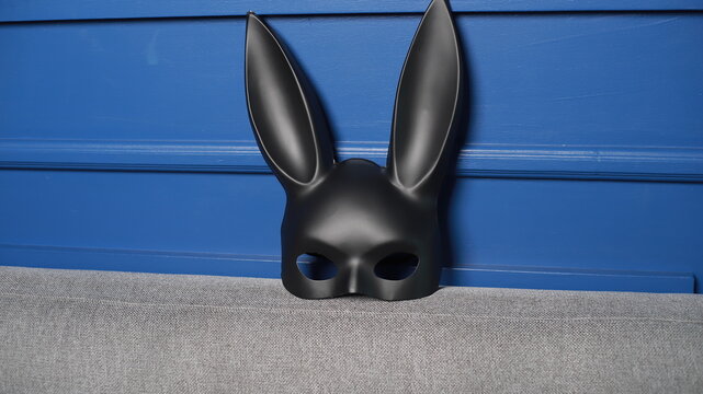 M&aacute;scara de conejo de cuero negro fetiche para jugar rol sobre un sofa de la sala junto a la pared azul