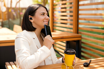 A person is sitting at a table outside in a cafe with a phone in his hand and a thoughtful look. A...