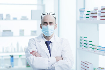 Pharmacist is Working in protective mask. Man Wearing Special Medical Uniform. Located in Pharmacy.