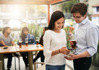 We look so funny in the picture. Shot of two cheerful young business work colleagues looking at photos on a phone outside at a restaurant.