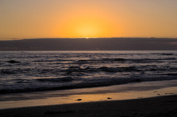 puesta de sol y ocaso en la orilla de playa con nubes en el horizonte y un pequeño bote