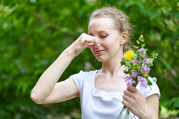 Allergy. Woman squeezed her nose with hand, so as not to sneeze from the pollen of flowers