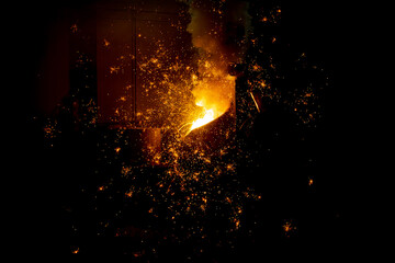 Foundry. Pouring hot metal from a ladle into molds. Bright red metal and sparks flying to the sides