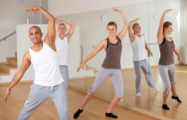 Portrait of positive hispanic man practicing classic dance moves during group class in studio