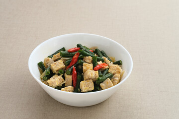 Oseng tempe kacang panjang or stir fried tempeh and long bean, Indonesia traditional cuisine, served on white bowl. Selected focus.
