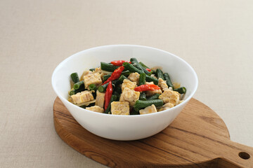 Oseng tempe kacang panjang or stir fried tempeh and long bean, Indonesia traditional cuisine, served on white bowl. Selected focus.
