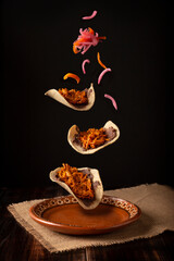 Creative food image of Mexican Tacos de Cochinita Pibil and onion with habanero chili falling on traditional mexican clay dish. Levitation photography. - 496975869