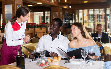 Waitress making recommendation to positive interracial couple having date in restaurant