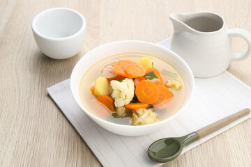 Sayur sop ( Soup) or vegetable  soup, is an Indonesian food. Served on white bowl on wooden background, close up.
