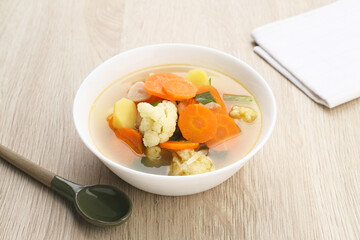 Sayur sop ( Soup) or vegetable  soup, is an Indonesian food. Served on white bowl on wooden background, close up.
