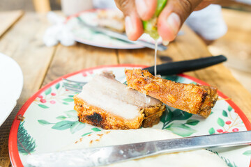 Closeup of the hand of a Latin woman seasoning a piece of chicharron with a squeeze of lime in a...